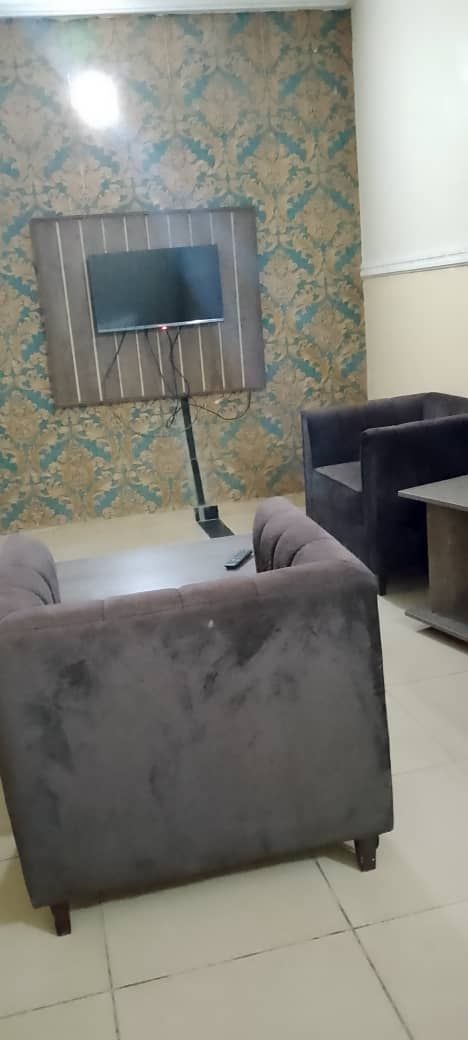 A room with a large flat-screen TV mounted on the wall, a dark-colored sofa, and a small table.
