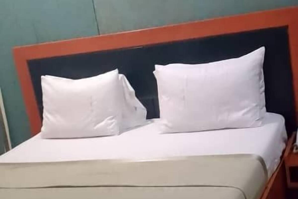 Ein Bett mit hölzernem Kopfteil und weißer Bettwäsche in einem Zimmer mit türkis-blauen Wänden und gefliestem Boden.