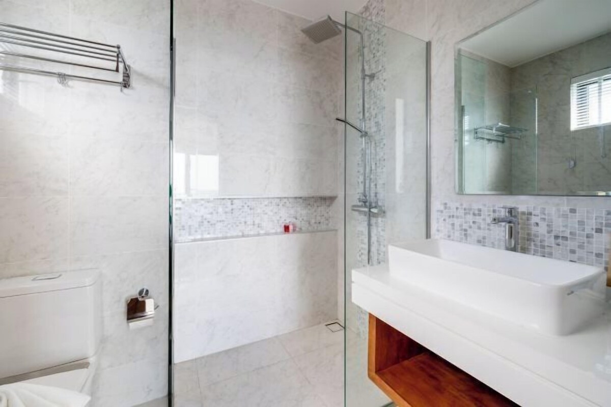 Un baño moderno con cabina de ducha de vidrio, un lavabo blanco y un espejo grande.