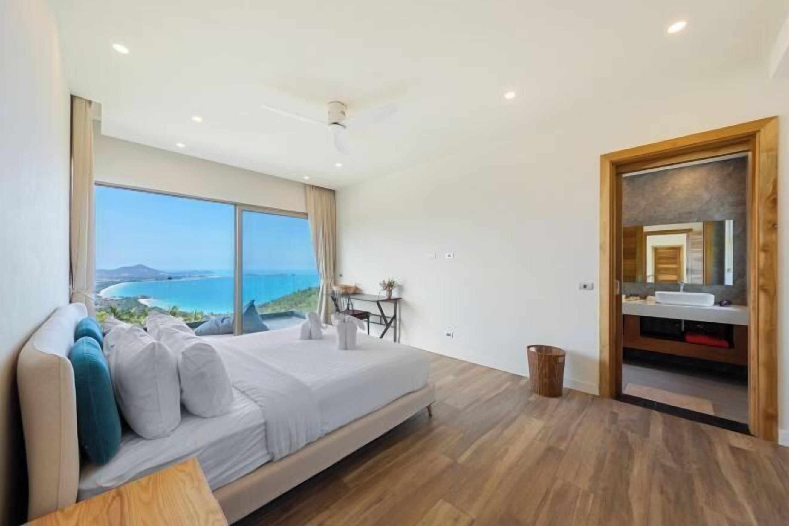 Ein Schlafzimmer mit großem Fenster, einem Bett, einem Schreibtisch und Blick auf den Ozean.