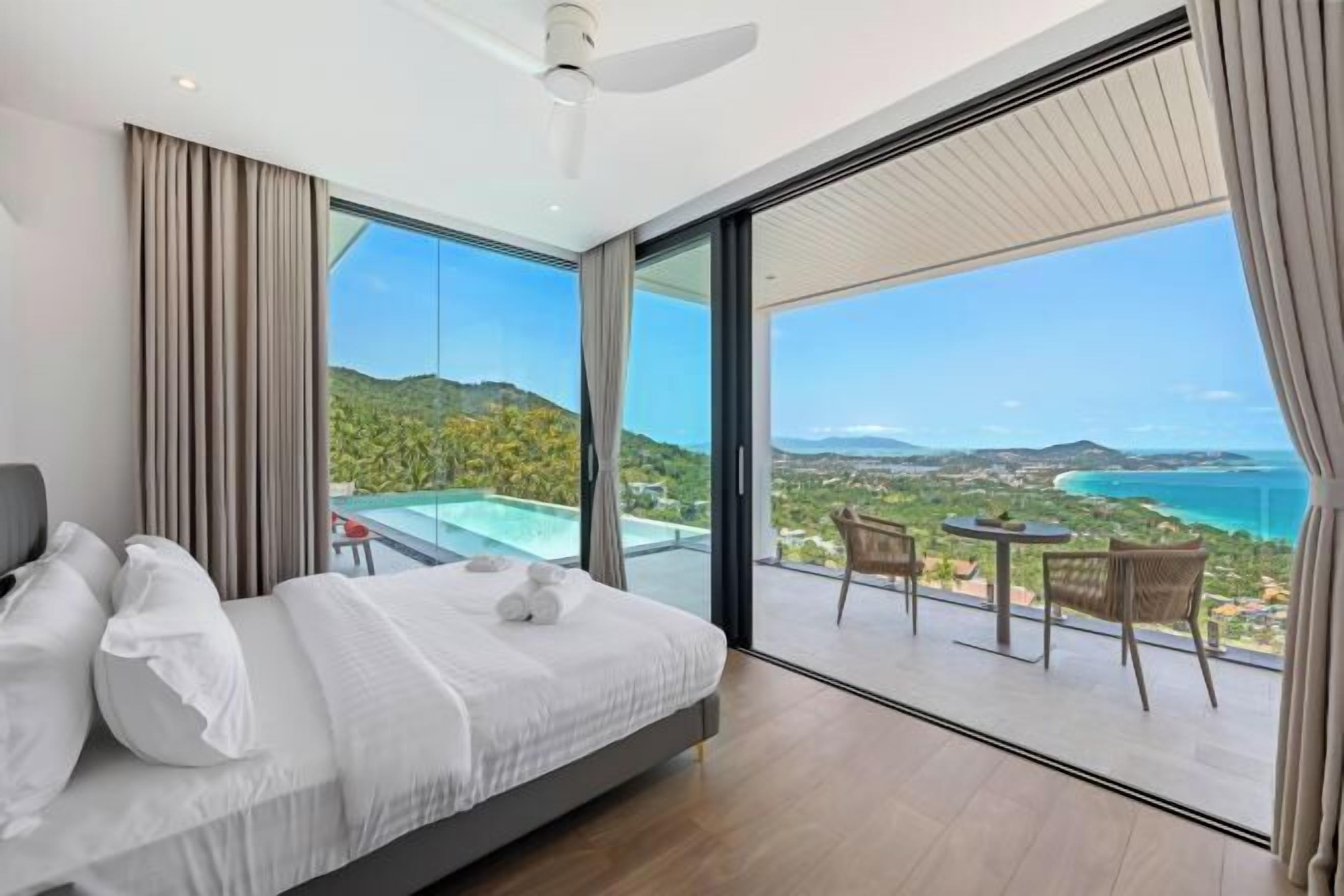 Ein Schlafzimmer mit einem großen Bett, einem Deckenventilator und einem Balkon mit Tisch und Stühlen.