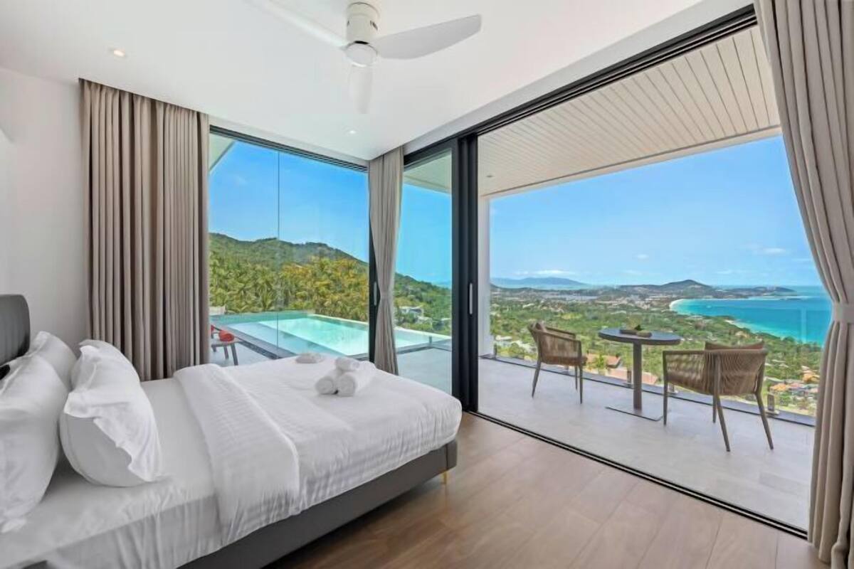 A bedroom with a large bed, a ceiling fan, and a balcony with a table and chairs.