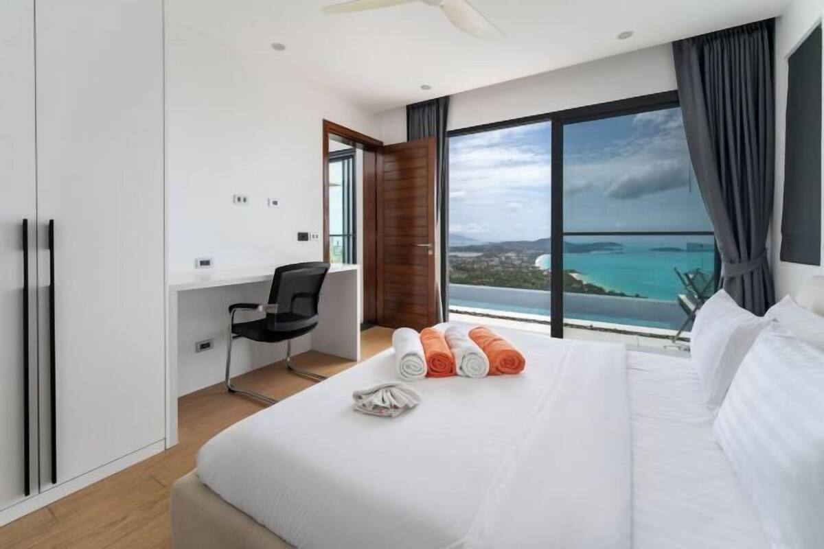 A modern hotel room with a large bed, a desk, and a view of the sea.