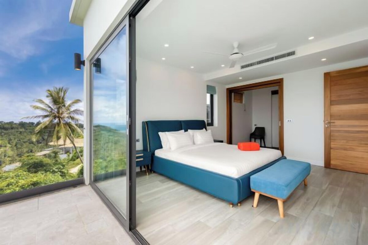A modern bedroom with a large bed, a bench, and a view of the outdoors.