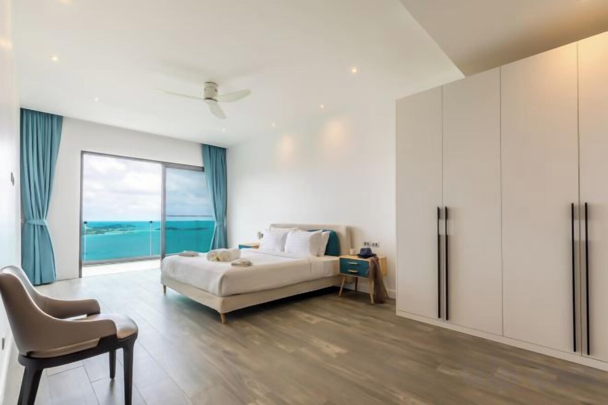 A modern bedroom with a bed, a chair, a nightstand, and a view of the ocean.
