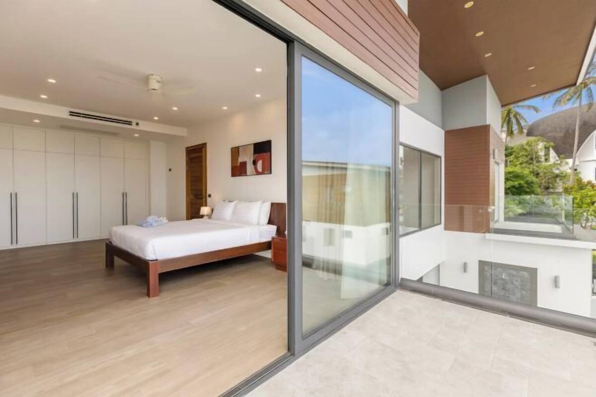 A modern bedroom with a large bed, a sliding glass door to a balcony, and a view of the outdoors.