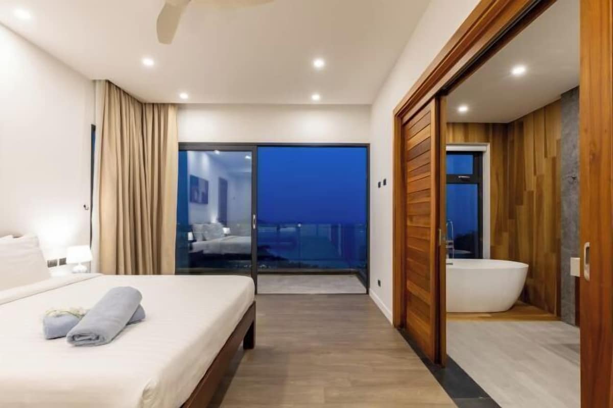 A modern hotel room with a bed, a bathroom with a bathtub, and a balcony with a view.