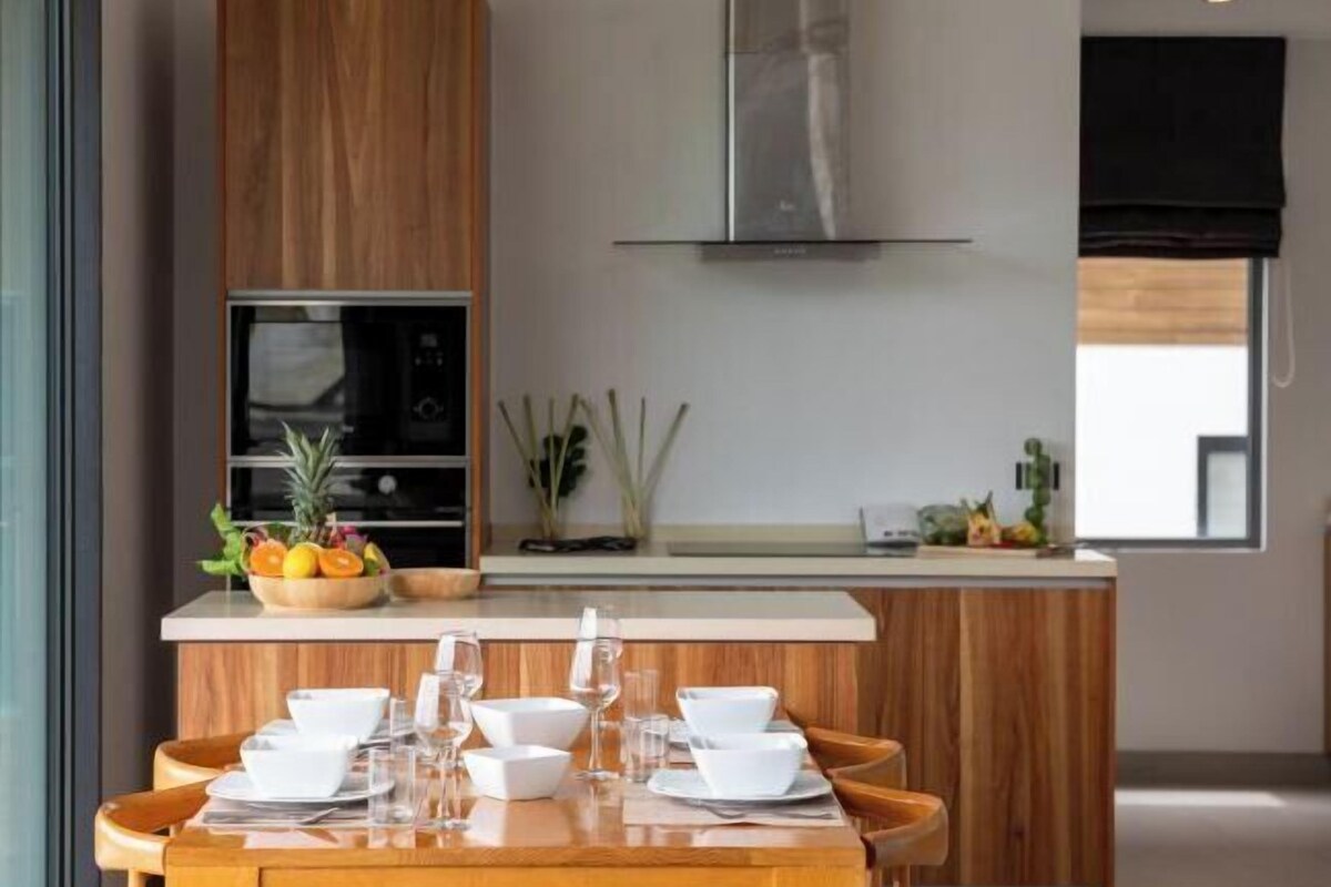 Una cocina moderna con una isla central, armarios de madera y una campana extractora de acero inoxidable.