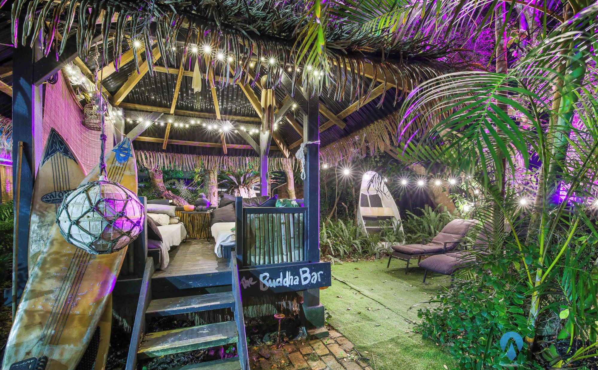 Tunnelmallinen ulkoalue, jossa on mukavat istuimet ja kyltti, jossa lukee ”Buddha Bar”. Alue on vehreän kasvillisuuden ympäröimä, ja sitä koristavat valosarjat.