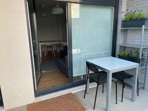A glass door leading to a dining area with a table and chairs, a small rug, and a metal shelf with plants.