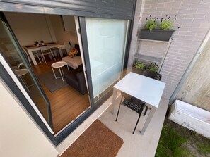 A modern outdoor patio area with a white table and chairs, a small seating area with a sofa and a coffee table, and a brick wall with potted plants.
