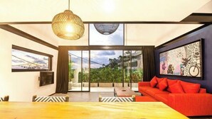 Un salon moderne avec une table à manger en bois, un canapé rouge et de grandes fenêtres donnant sur un paysage verdoyant.