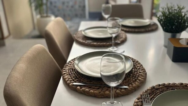 Una mesa de comedor dispuesta con platos, cubiertos y vasos, rodeada de sillas.