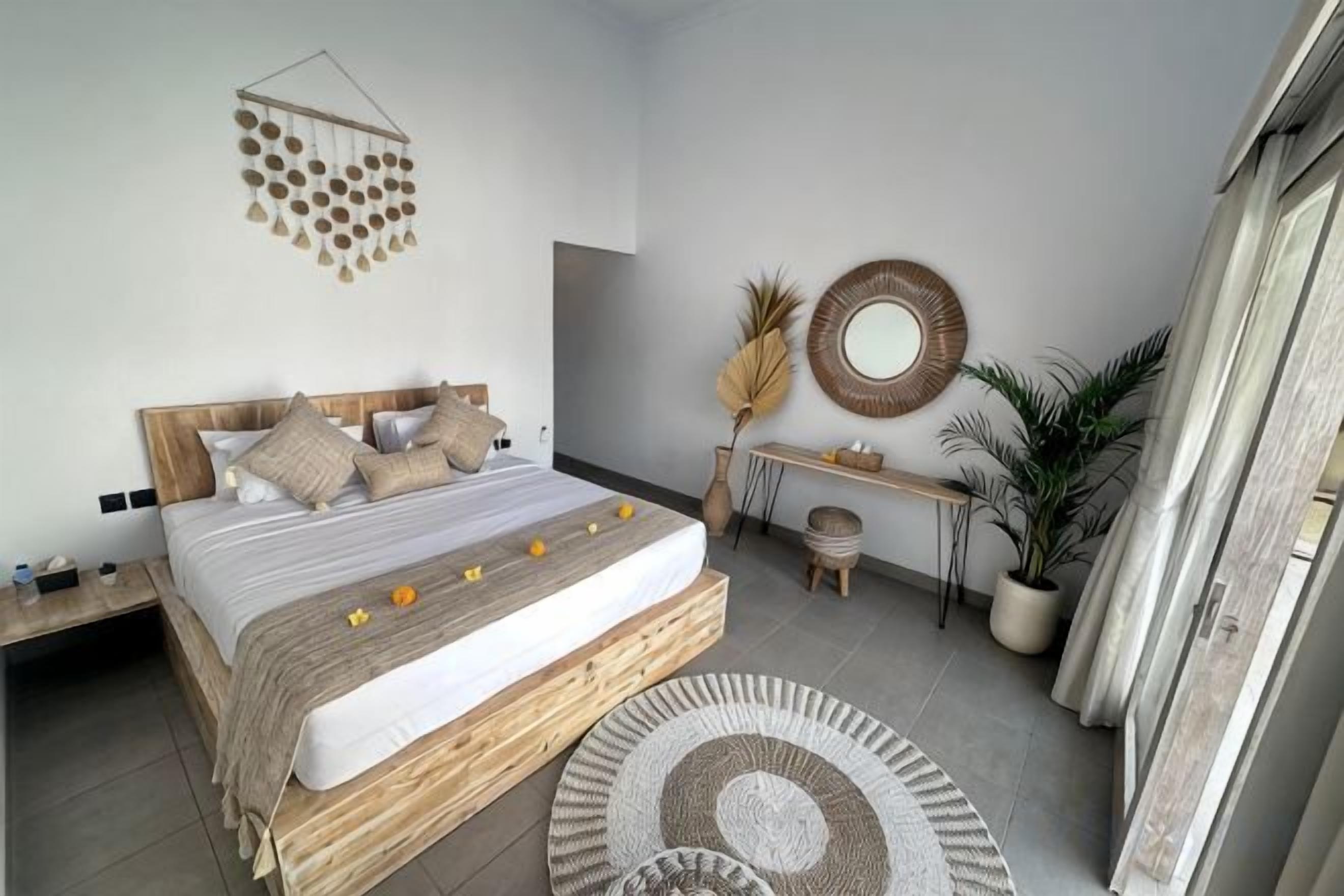 A bedroom with a wooden bed, bedside tables, a round mirror, a small desk, and a potted plant.
