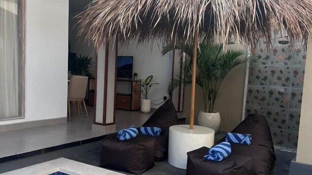 Un área de piscina interior moderna con dos sillones de exterior, una pequeña mesa redonda y una planta grande en maceta.