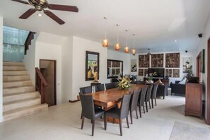 A spacious dining area with a long wooden table, multiple chairs, and pendant lighting.