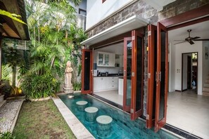 A modern house with a swimming pool, a statue, and a kitchen visible through glass doors. - Villa Annecy, Fully Staffed Luxury Villa Central Seminyak (Bali)