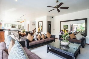 A spacious living area with a sofa set, a coffee table, and a dining area in the background.