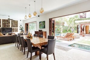 A modern dining area with a wooden table, chairs, and a TV. - Villa Annecy, Fully Staffed Luxury Villa Central Seminyak (Bali)