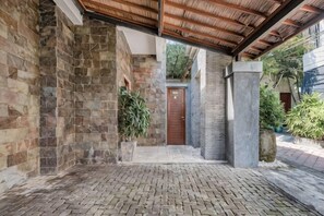 Un espace extérieur abrité, doté de murs en pierre, d’un sol en briques et d’une porte en bois.