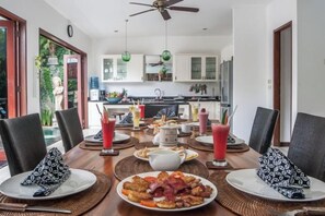 Un coin repas avec une table dressée pour quatre personnes, une cuisine en arrière-plan et un ventilateur de plafond.