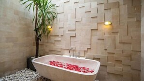 Une baignoire remplie de pétales de rose, une plante en pot et un mur orné d’un motif géométrique.