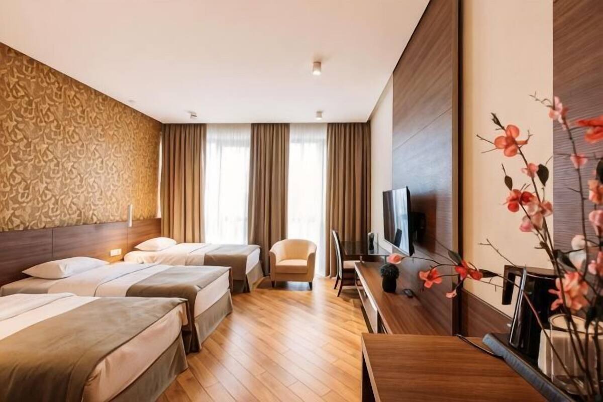 A hotel room with three beds, a TV, a desk, and a chair.