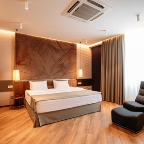 A modern hotel room with a large bed, a side table, a chair, and a large window with curtains. - Hotel Tbilisi Tower (Tbilisi)