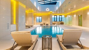 Una piscina interior moderna con techo de tragaluces, sillas de descanso y vistas a las montañas.