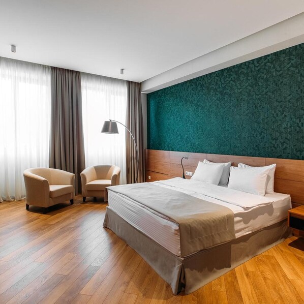 A hotel room with a large bed, two armchairs, a desk, and a green patterned wall. - Hotel Tbilisi Tower (Tbilisi)