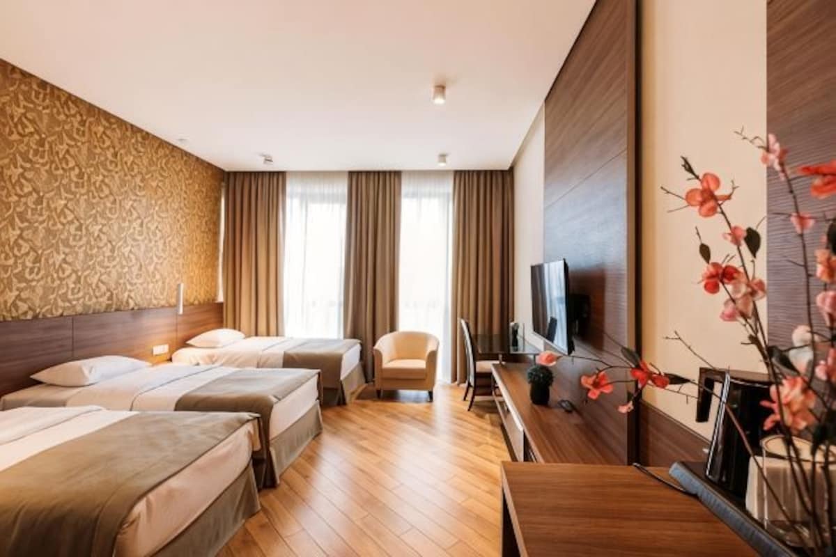 A hotel room with three beds, a TV, a desk, and a chair.