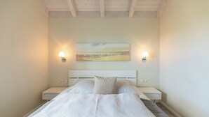 A neatly made bed with a white headboard, two bedside tables, and a painting above the bed. - Vacation home "Seemannsnest" in Dagebüll for up to 4 people (Dagebüll)