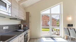 A modern kitchen with a built-in oven, a microwave, and a large window opening to a patio area. - Vacation home "Seemannsnest" in Dagebüll for up to 4 people (Dagebüll)