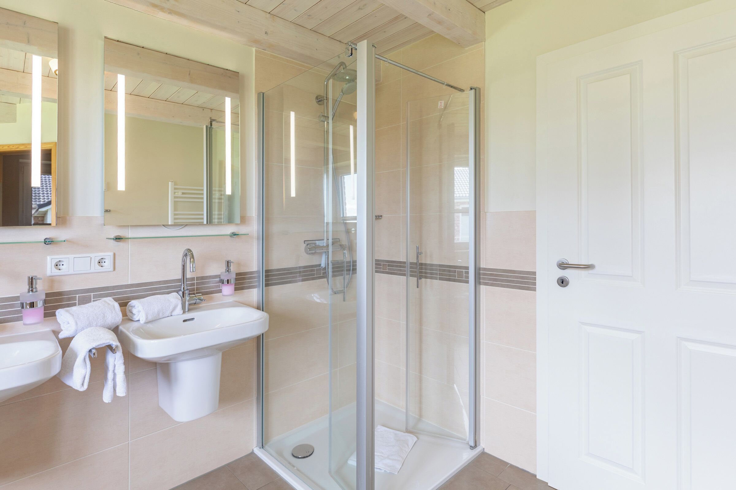 A modern bathroom with a glass-enclosed shower, two sinks, and a large mirror.