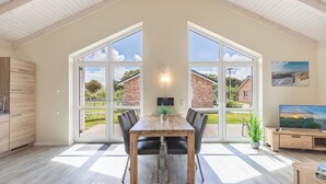 A spacious dining area with a wooden table and chairs, large windows offering a view of the outdoors, and a television on a wooden stand. - Vacation home "Seemannsnest" in Dagebüll for up to 4 people (Dagebüll)