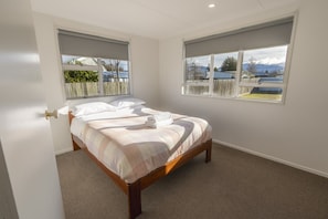 A bedroom with a bed, two windows, and a view of a fenced yard.