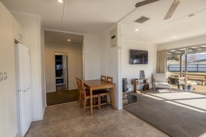 A modern living room with a wooden dining table, a sofa, and a TV mounted on the wall.