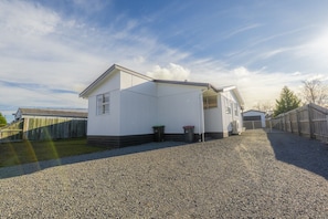 A single-story white building with a gravel driveway, a wooden fence, and a clear sky.