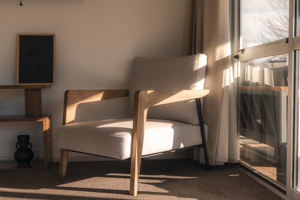 A modern chair with wooden legs and a cushioned seat, positioned near a window with curtains.