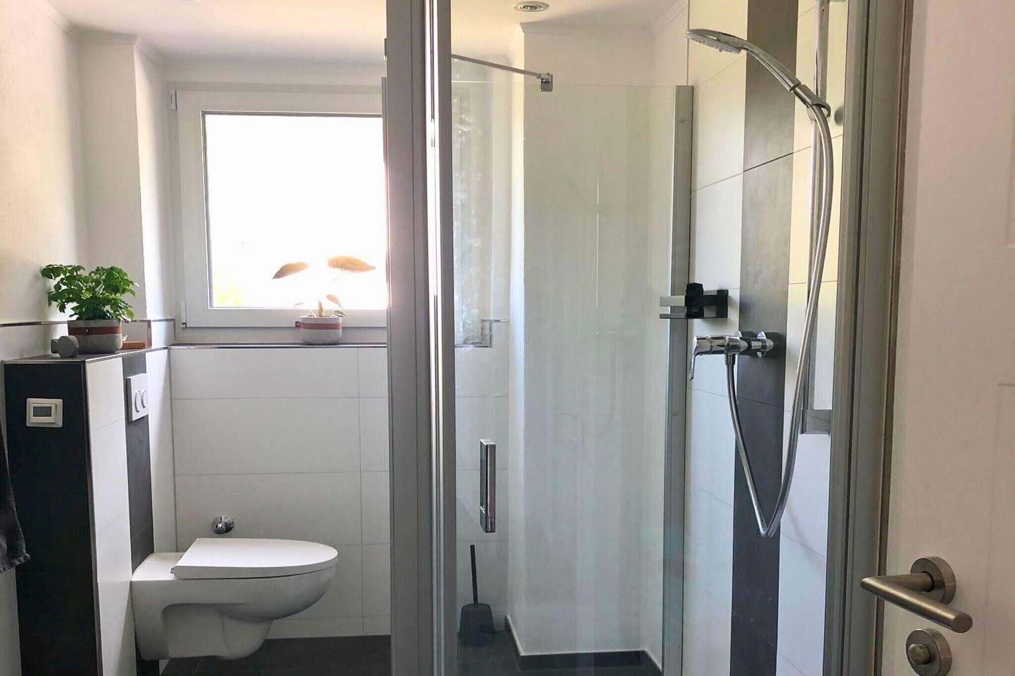 A modern bathroom with a glass-enclosed shower, a toilet, and a window.
