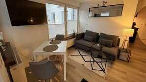 Un salon avec une table blanche, un canapé gris et un téléviseur fixé au mur.