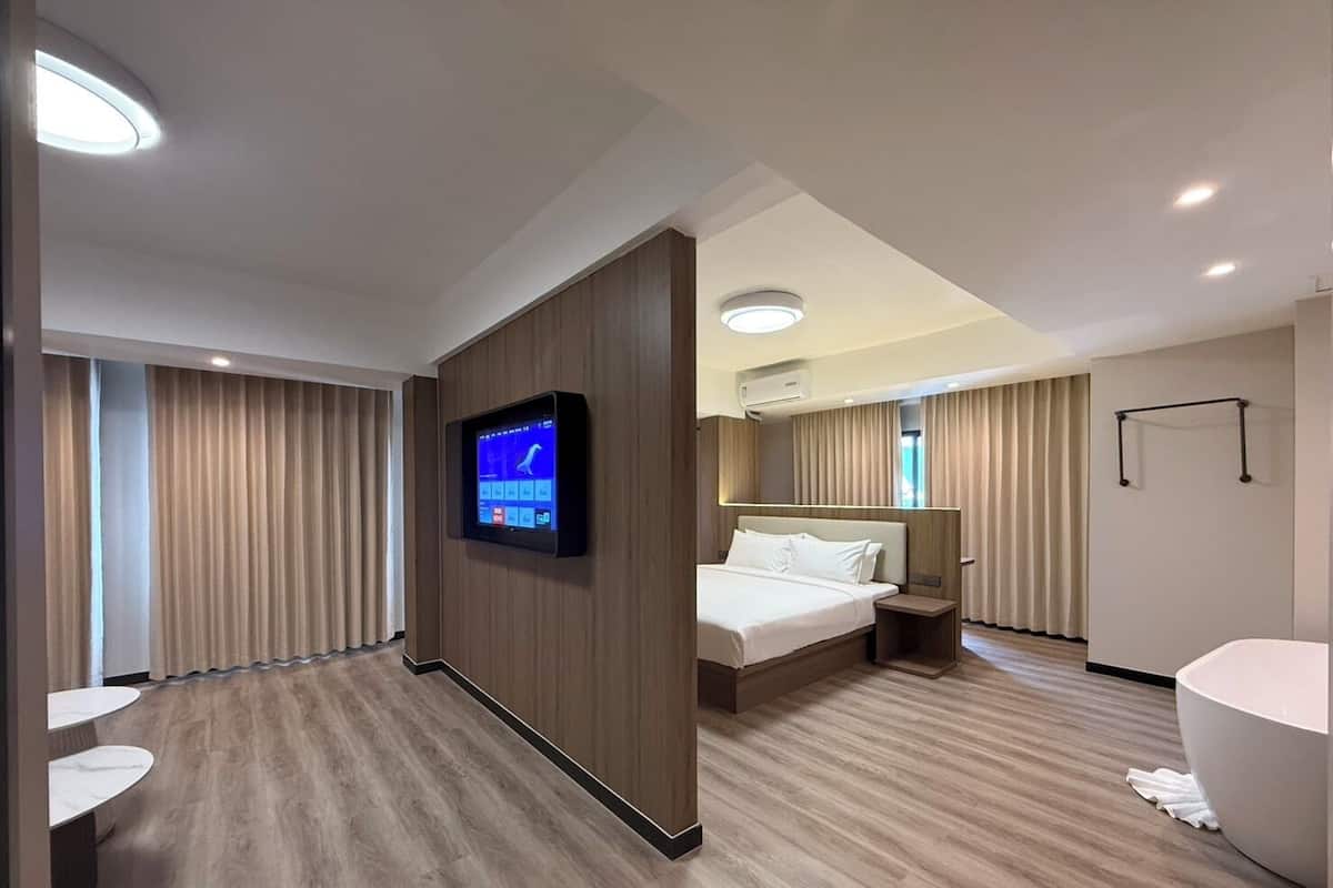 Una moderna camera d'albergo con un letto grande, una televisione a schermo piatto fissata al muro, un bagno con vasca e un pavimento in legno.