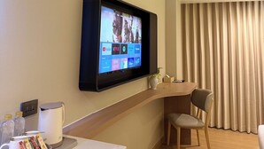 A hotel room with a flat-screen TV mounted on the wall, a small table with a tray of snacks, a chair, and a large window with curtains. - Star Hotel Pattaya (Pattaya)