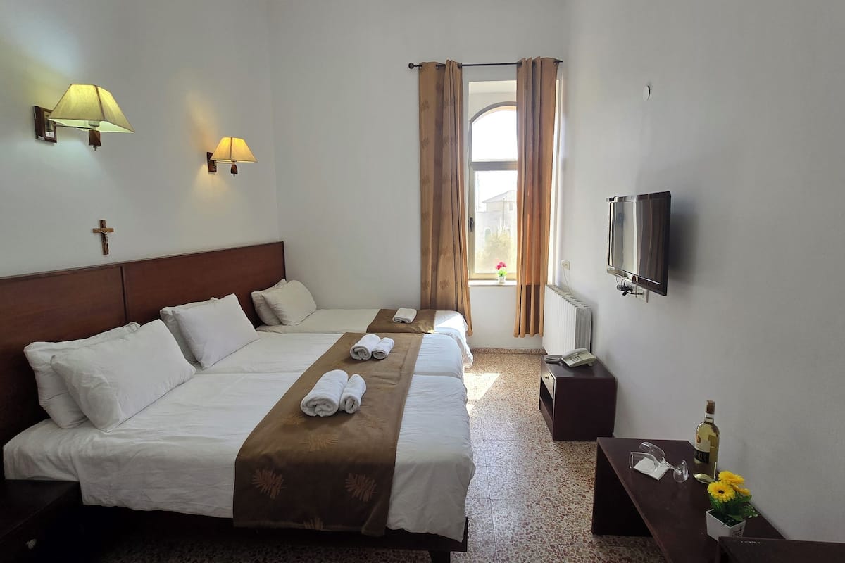 A hotel room with two beds, a TV, a telephone, and a window with curtains.