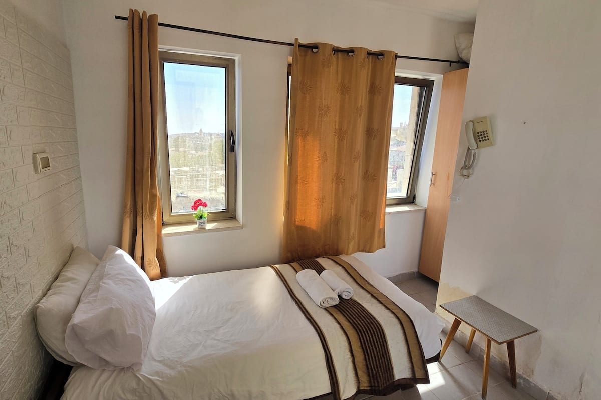 A bedroom with a bed, a small table, and a window with curtains.