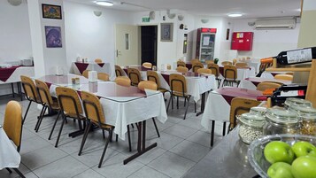 Un área de comedor con varias mesas y sillas, un letrero de salida, una máquina expendedora y un refrigerador.