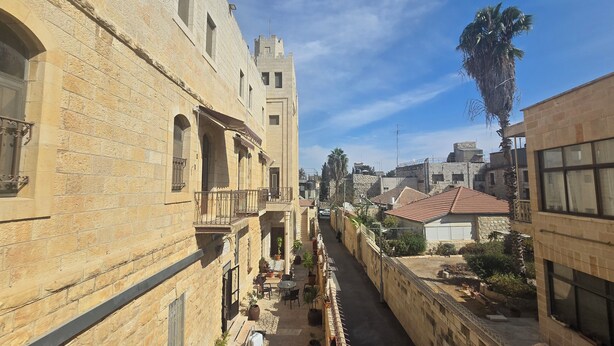 A narrow alleyway flanked by stone buildings with balconies and outdoor seating areas.