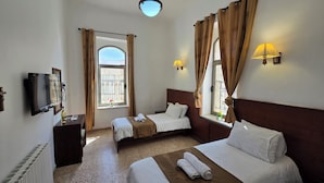 A hotel room with two beds, a TV, a window with curtains, and a wall-mounted lamp.