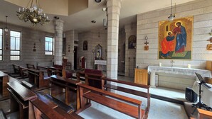 A church interior with wooden pews, stone columns, a chandelier, and religious artwork.