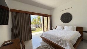 A bedroom with a large bed, a desk, and a view of a garden through an open door. - Octa House (Kutuh)